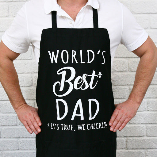 Black BBQ apron printed with World’s Best Dad slogan, displayed on outdoor setting