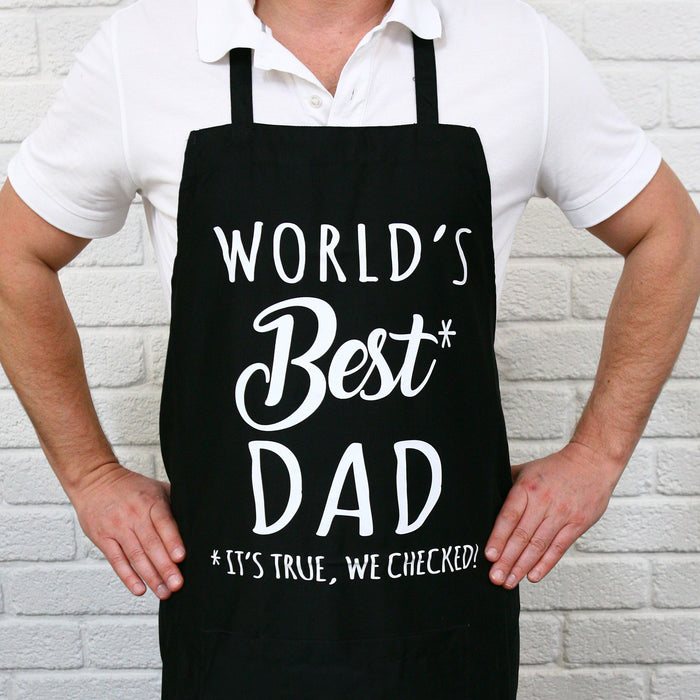 Black BBQ apron printed with World’s Best Dad slogan, displayed on outdoor setting