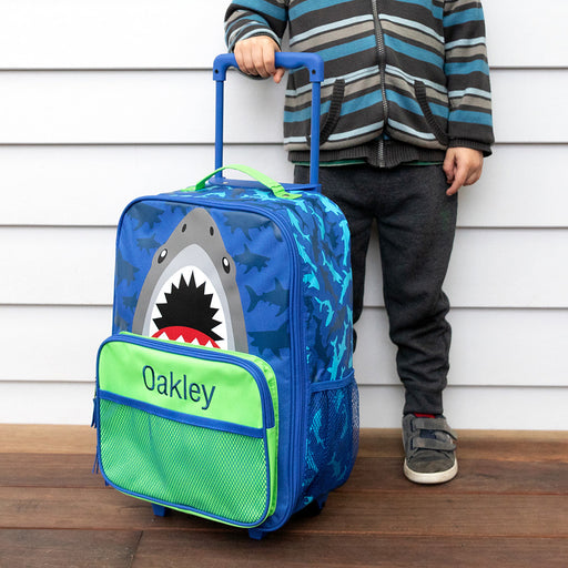 Child standing next to custom shark rolling suitcase with extended handle.
