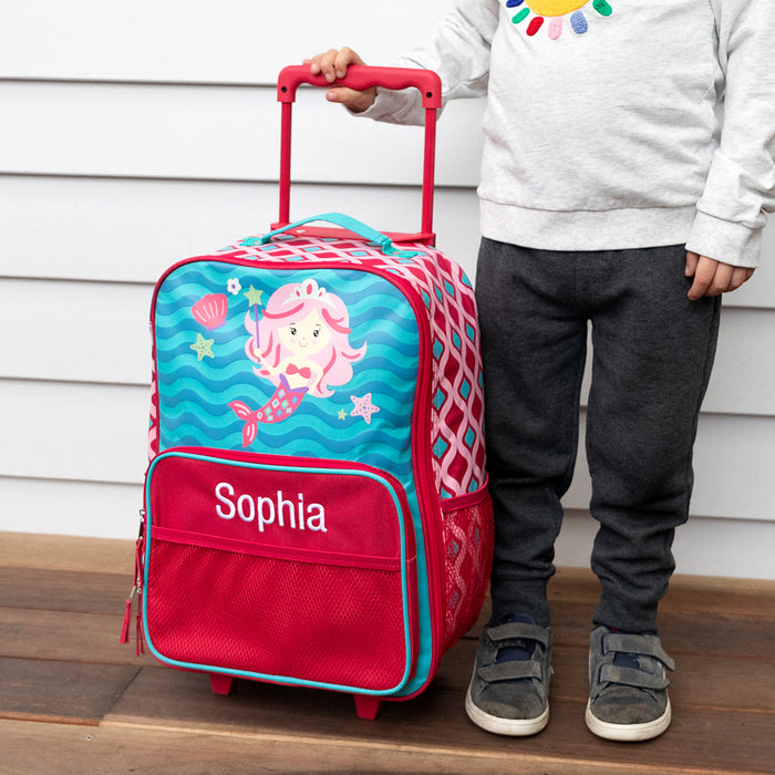 Child standing beside a custom mermaid rolling suitcase with extendable handle.