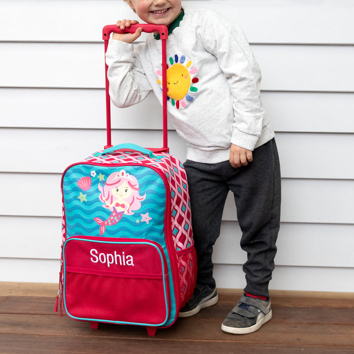 Smiling child holding personalised mermaid trolley case with embroidered name and extended handle, ready for travel or school adventure.