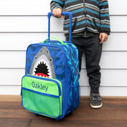 Child standing next to custom shark rolling suitcase with extended handle.
