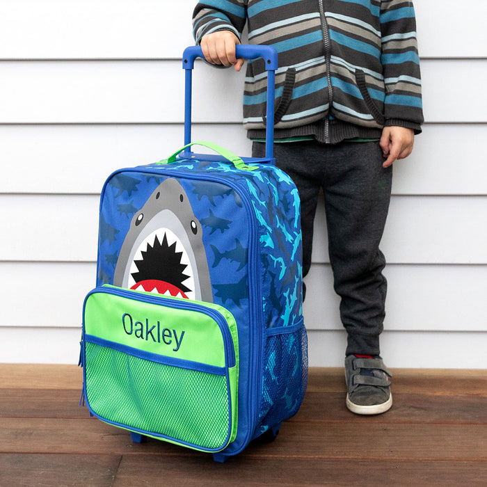 Child standing next to custom shark rolling suitcase with extended handle.