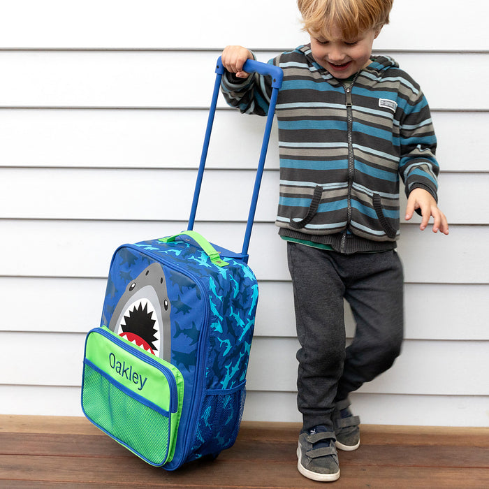 Child happily pulling personalised shark suitcase with name embroidery and ocean print.