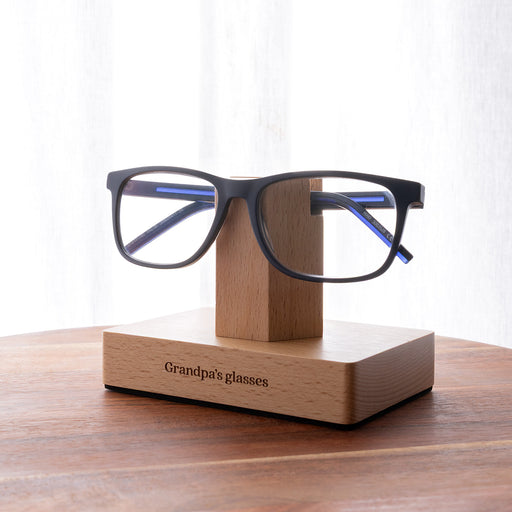 Personalised beech wood reading glasses stand engraved with a name, holding one pair of glasses on a bedside table.